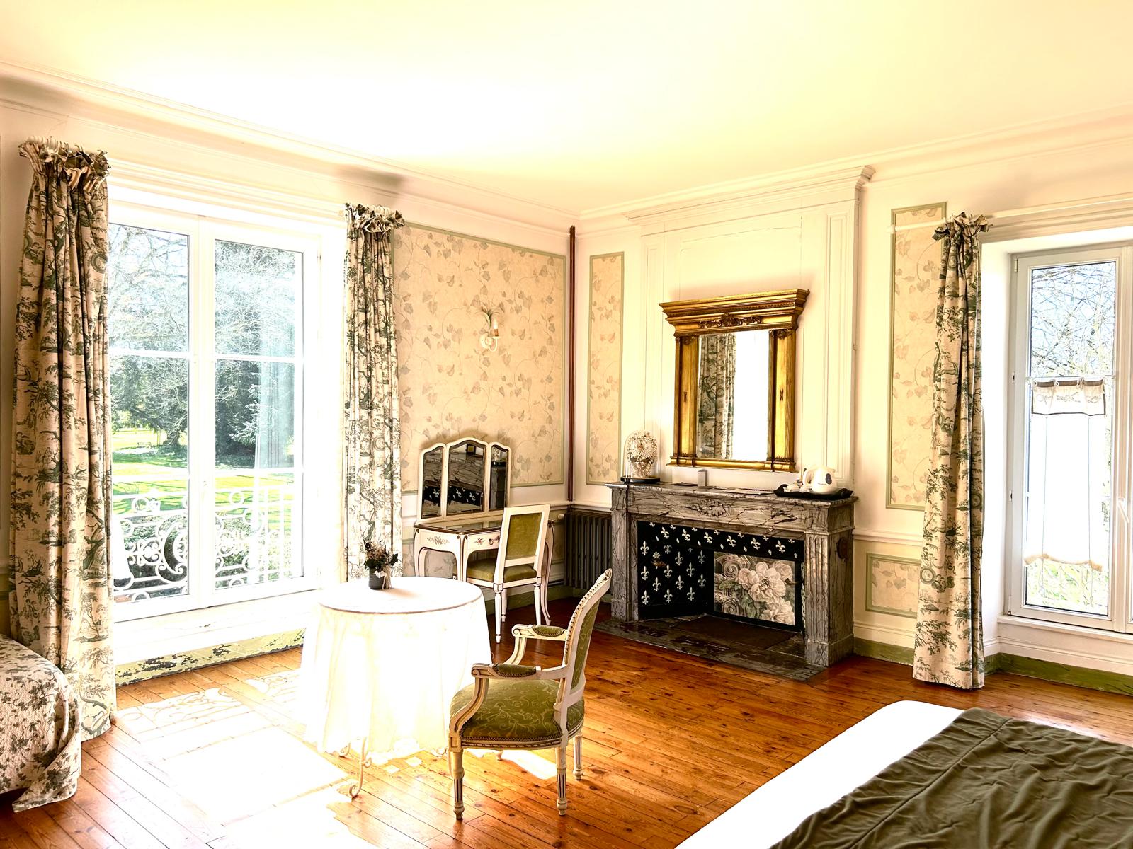 La décoration de la chambre Queen et Ange avec sa table pour se poser, sa coiffeuse et sa cheminée. Des couelurs très sobres (blanc, beige, marron) et une touche de vert.